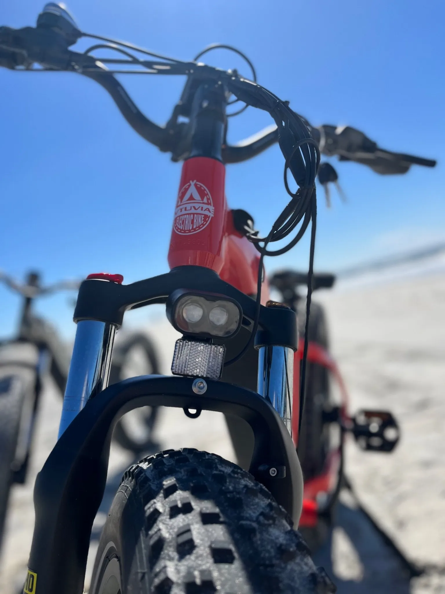 Close-up of a red e-bike’s LED headlight, handlebars and knobby fat front tire