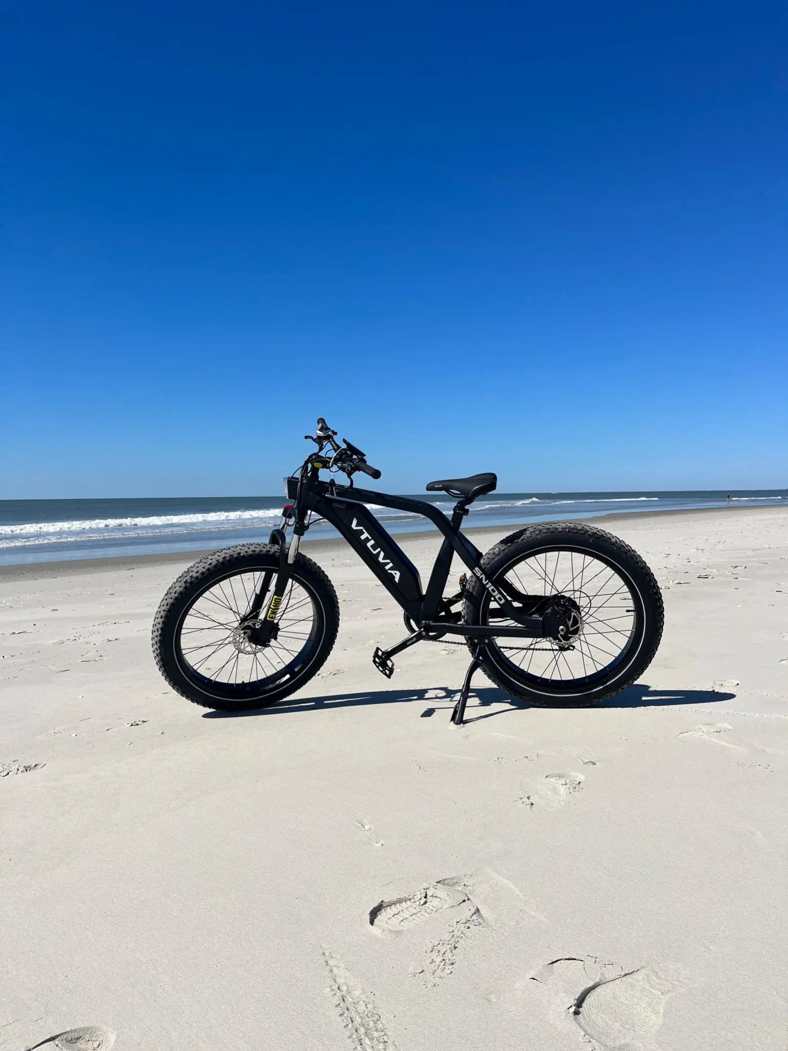 Black fat-tire step-through e-bike standing on the sand in front of the ocean