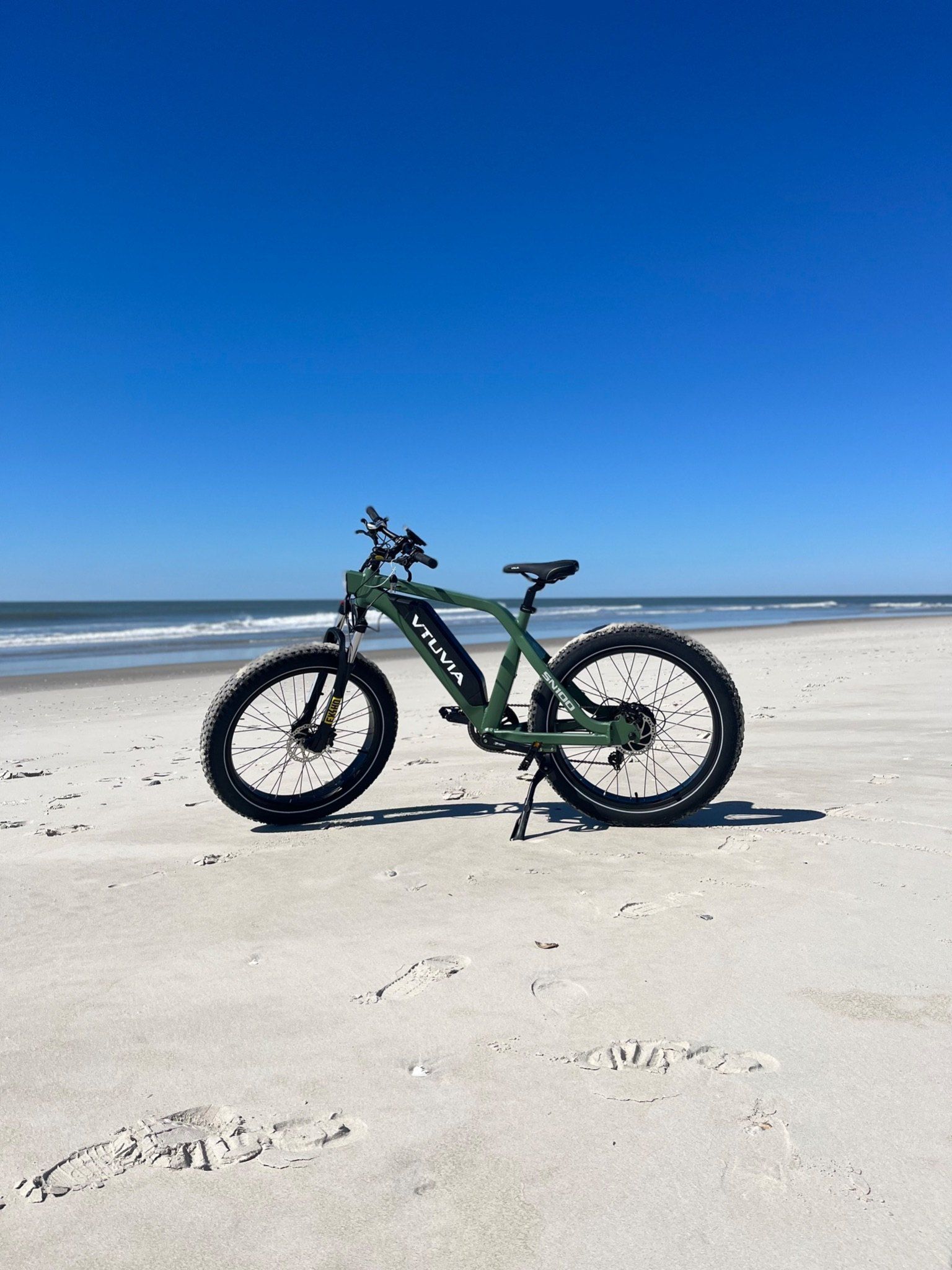 Green fat-tire step-through e-bike standing on the sand in front of the ocean