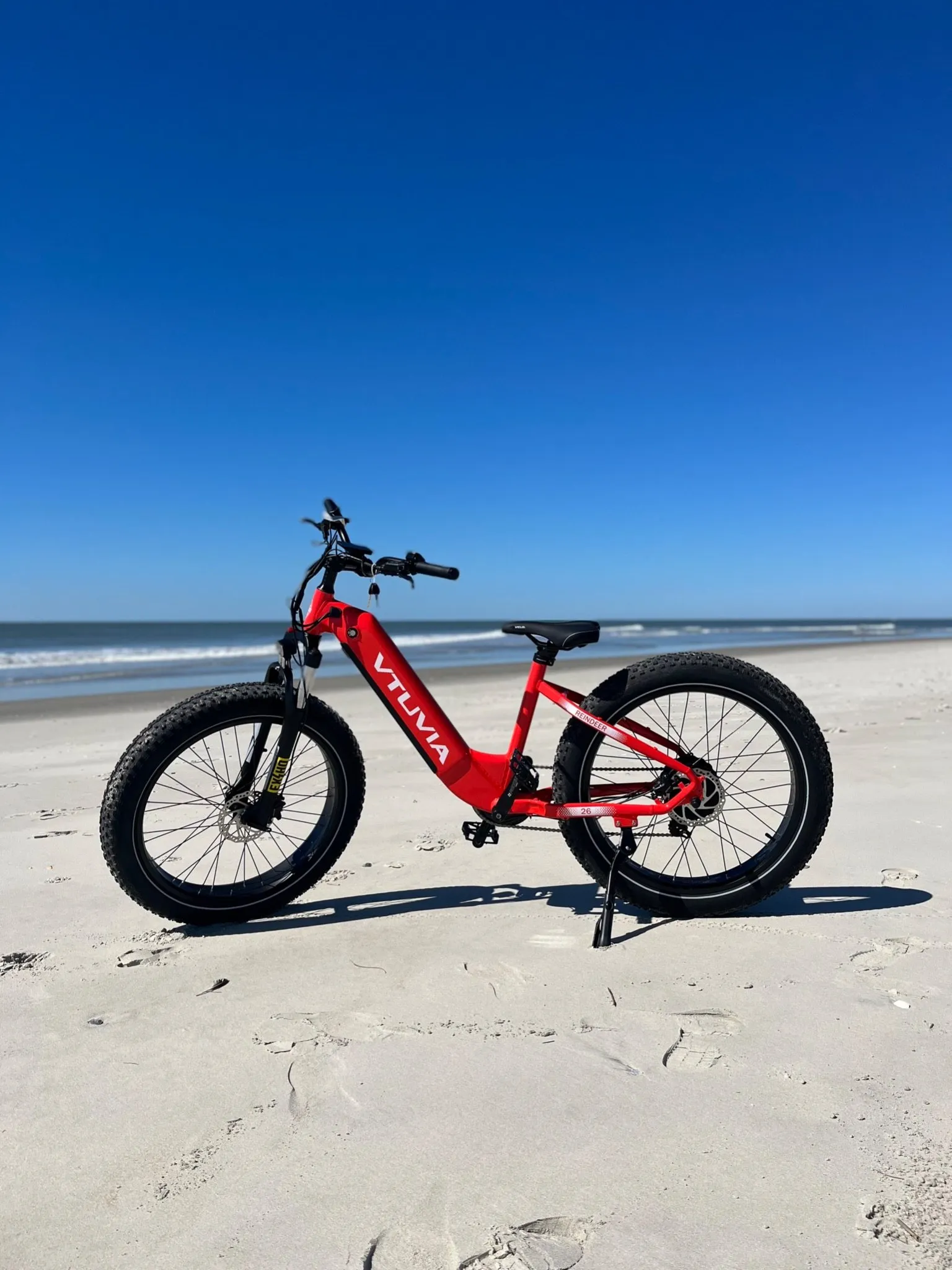 Red fat-tire step-through e-bike standing on the sand in front of the ocean